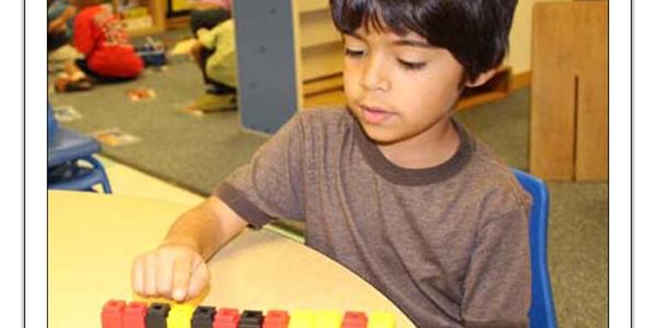 Boy sitting at table playing with small, multicolored blocks